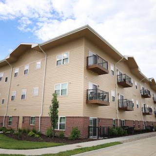 A multi-unit apartment building with balconies and landscaped grounds under a cloudy sky.