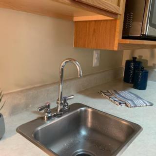 A modern kitchen with a stainless steel sink and faucet, featuring neatly arranged countertop items and wooden cabinets.