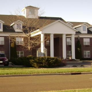 A large brick residential building with white columns and a landscaped front yard.
