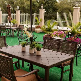 A peaceful outdoor patio with metal tables and chairs, surrounded by lush greenery and potted plants.