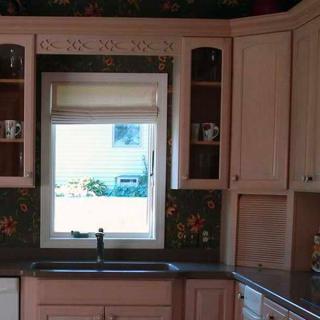 A kitchen with light-colored cabinets, a central window above the sink, and decorative wallpaper.