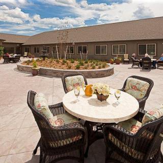 A cozy outdoor patio area with a round table and chairs, surrounded by garden beds under a clear blue sky.