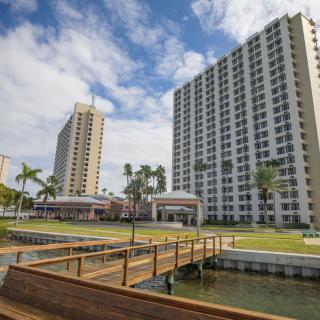 High-rise residential buildings with palm trees and a wooden walkway under a cloudy sky.
