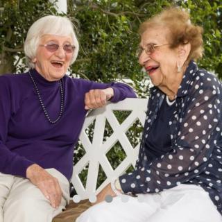 Two elderly women enjoying a joyful conversation on a park bench.