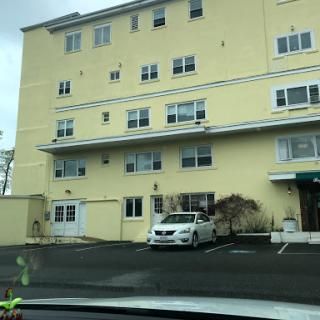 A yellow residential building with multiple windows and a parked vehicle in the lot.