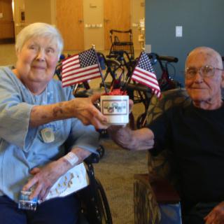 An elderly couple enjoying a moment together, holding a coffee mug and surrounded by American flags in an indoor setting.
