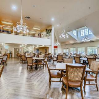 A spacious dining area with elegant chandeliers, wooden tables, and chairs on polished wood flooring.