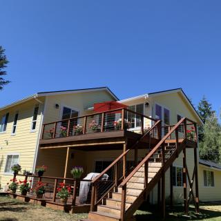 A two-story house with a wooden deck and staircase leading to the backyard on a sunny day.
