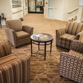 A cozy lobby seating area with patterned armchairs and a round table on a carpeted floor.