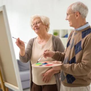 An elderly couple painting together at an easel.