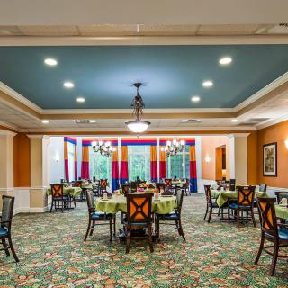 A well-lit dining area featuring multiple tables set with chairs, vibrant carpet, and elegant decor.