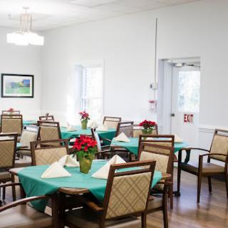 A well-lit dining area set up for a gathering, featuring tables adorned with green tablecloths and decorative plants.