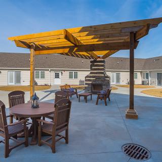 A spacious patio area featuring wooden furniture, a pergola, and an outdoor fireplace.