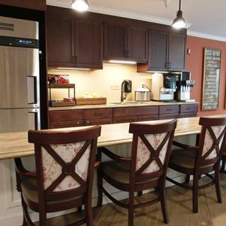 A modern kitchen with a counter and wooden chairs, featuring sleek appliances and warm lighting.