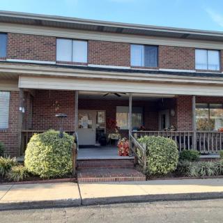 A two-story brick residential house with a porch and well-maintained shrubs.
