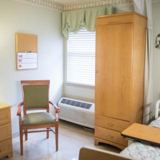 A neatly arranged room featuring a chair, wardrobe, and a window with natural light.