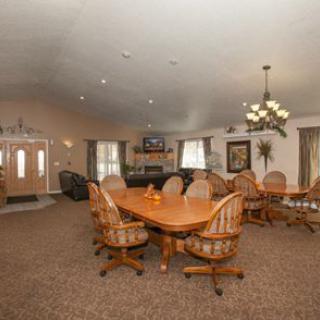 A spacious dining room with a large wooden table and chairs, decorated with a chandelier and carpeted flooring.