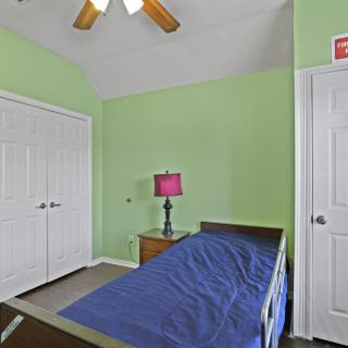 A cozy bedroom with green walls, featuring a single bed, a lamp on a bedside table, and a ceiling fan.
