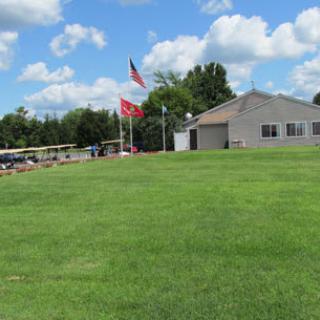 A building with flags and a large green lawn under a cloudy sky.