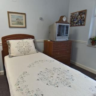 A cozy bedroom with a single bed, floral bedspread, and a TV on a wooden dresser.