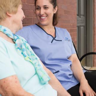 A nurse and an elderly woman smiling and conversing outdoors.