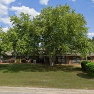 A suburban house surrounded by trees with a well-kept lawn under a partly cloudy sky.