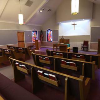 A peaceful church interior with pews, an altar, and stained glass windows.