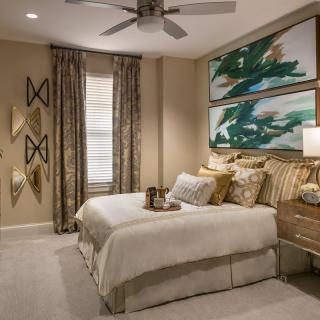 A modern bedroom featuring elegant decor with a comfortable bed, artistic wall hangings, and a ceiling fan.