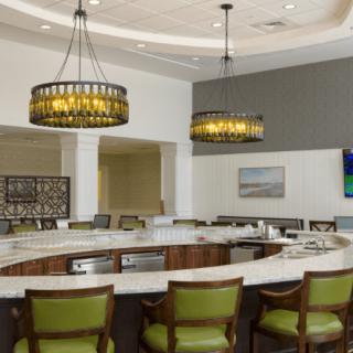 A modern kitchen bar area with pendant lighting and green upholstered chairs.