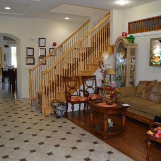 A cozy living room with a staircase, featuring wood and tile flooring, classic furniture, and decorative elements.