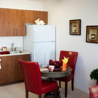 A cozy kitchen and dining area with red chairs and wooden cabinetry.