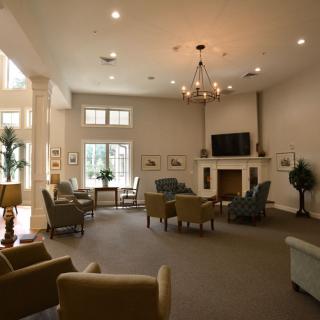 A spacious living room featuring comfortable seating, a fireplace, and a mounted TV, illuminated by natural light from large windows.