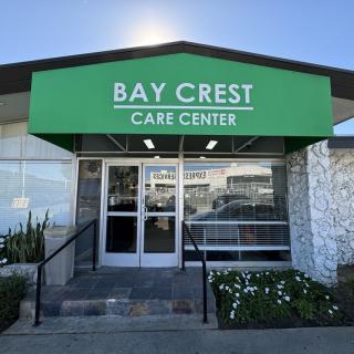 The entrance of Bay Crest Care Center with a green awning and surrounding plants.