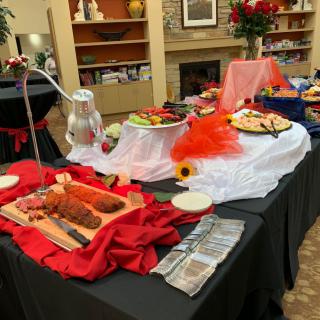A beautifully arranged buffet table with various dishes, decorated with colorful fabrics and accents, set up for an indoor event.