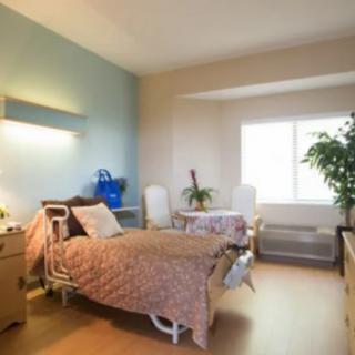 A hospital room with a patient bed, furniture, and a window letting in natural light.