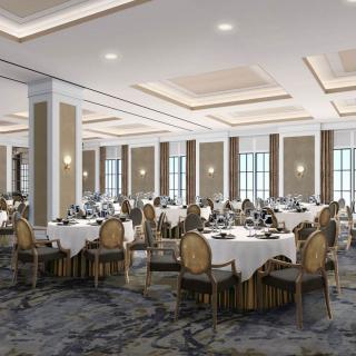 An elegantly set banquet hall ready for a formal event, featuring round tables with white tablecloths and decorative chairs.