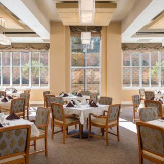 A bright and inviting dining area with neatly arranged tables and chairs, featuring large windows that allow natural light to fill the space.