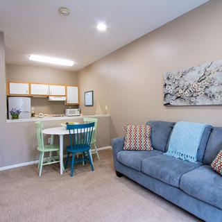 A cozy apartment with a living room and adjacent kitchen area, featuring a comfortable sofa and dining table.