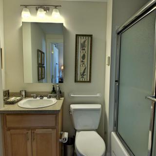 A small, well-lit bathroom with a vanity mirror, sink, toilet, and a shower with sliding glass doors.