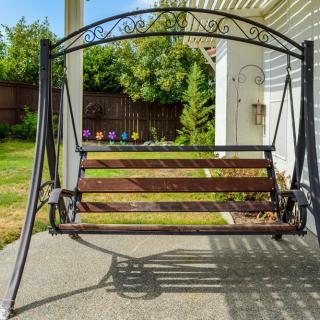 A garden swing with a wooden seat and metal frame on a patio.