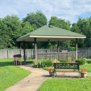A peaceful garden setting with a gazebo, bench, and lush greenery.