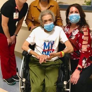 A group of healthcare workers posing with an elderly person in a wheelchair, all wearing masks.