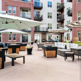 A modern apartment complex with an outdoor patio featuring stylish seating and large umbrellas.