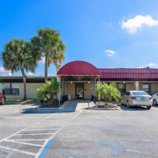 A single-story building with a red roof and palm trees in the parking lot under a clear blue sky.