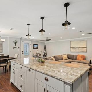 A modern open-concept kitchen and living room featuring a large island with granite countertops and pendant lighting.