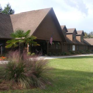 A wooden building with a series of peaked roofs surrounded by greenery and a well-maintained lawn.