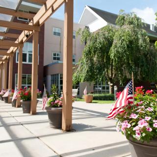 A sunlit pathway with potted flowers and American flags leading to a modern building.
