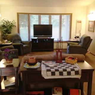 A cozy living room with two armchairs facing a TV, surrounded by wooden furniture and decorative items.