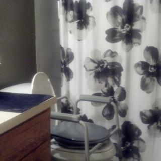 A bathroom featuring a floral-patterned shower curtain and a commode chair next to a sink.