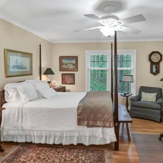 A cozy, traditional bedroom featuring a four-poster bed, armchair, and framed artwork.